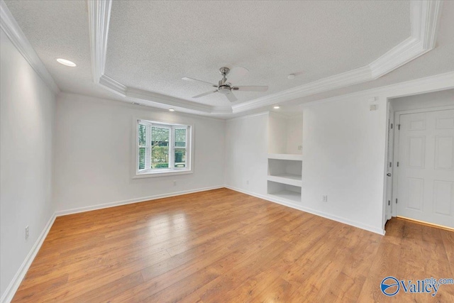 unfurnished room featuring built in features, light wood-style floors, a raised ceiling, and a textured ceiling