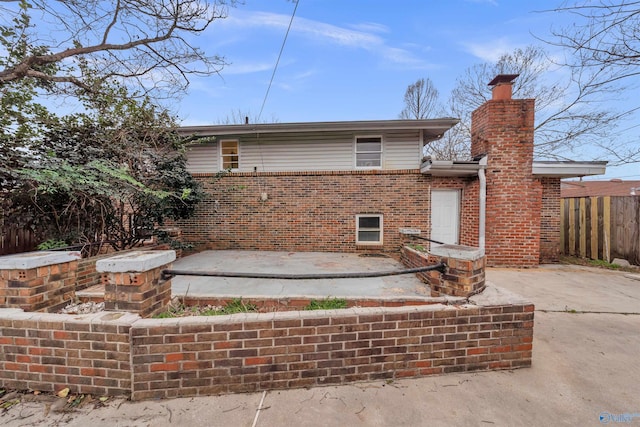 rear view of house featuring a patio area, a chimney, brick siding, and fence