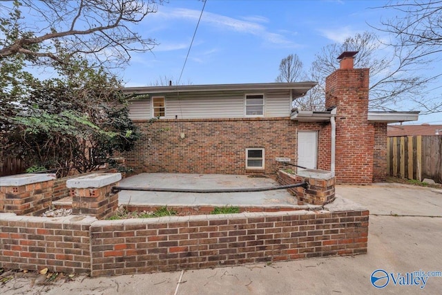 back of house with a patio, brick siding, a chimney, and fence