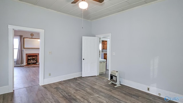 empty room with dark wood-type flooring, ceiling fan, a brick fireplace, and heating unit