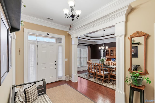 entryway featuring dark hardwood / wood-style flooring, crown molding, a chandelier, and ornate columns