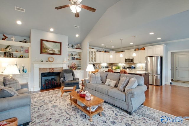 living room featuring a fireplace, light hardwood / wood-style floors, high vaulted ceiling, and ceiling fan