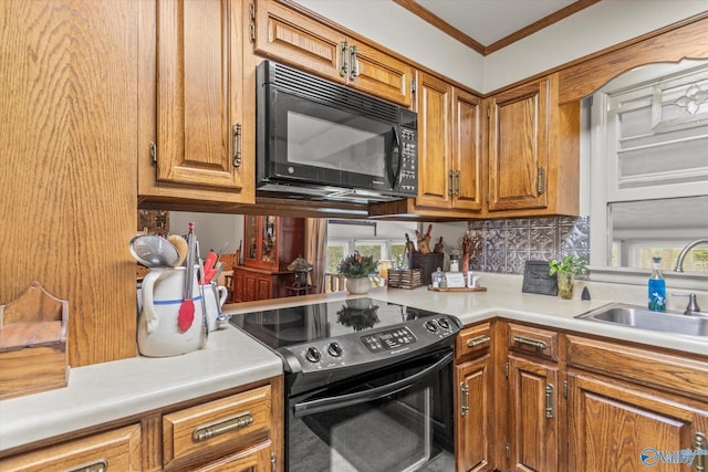 kitchen with a sink, light countertops, ornamental molding, brown cabinets, and black appliances