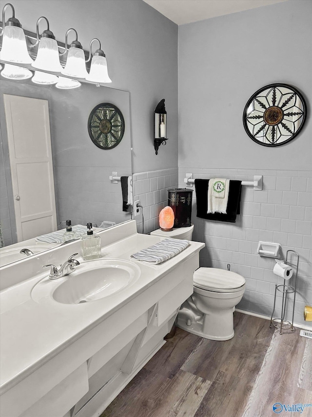 bathroom with wainscoting, toilet, wood finished floors, vanity, and tile walls