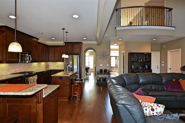 kitchen with pendant lighting, dark wood-type flooring, appliances with stainless steel finishes, a kitchen island, and a breakfast bar area