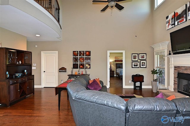 living room featuring a high ceiling, dark hardwood / wood-style floors, a stone fireplace, and ceiling fan