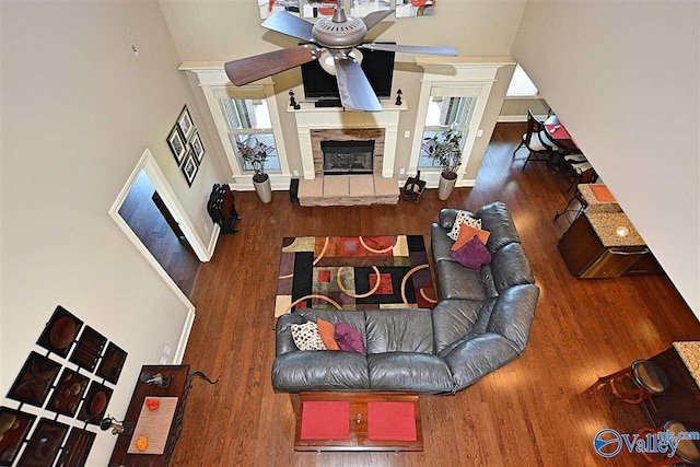 living room featuring a towering ceiling, hardwood / wood-style flooring, a stone fireplace, and ceiling fan