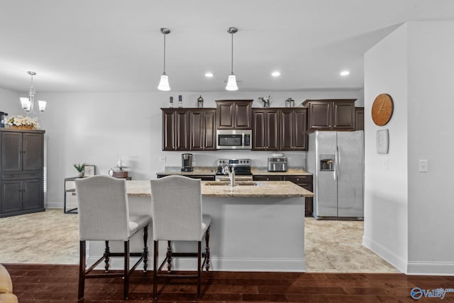 kitchen featuring light stone counters, a center island with sink, decorative light fixtures, and appliances with stainless steel finishes