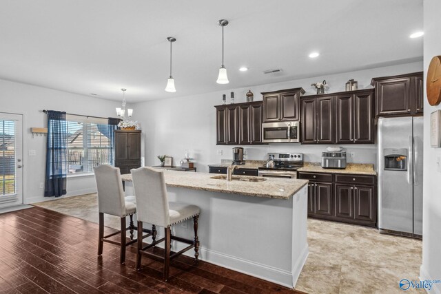 kitchen with sink, light hardwood / wood-style flooring, decorative light fixtures, a kitchen island with sink, and appliances with stainless steel finishes