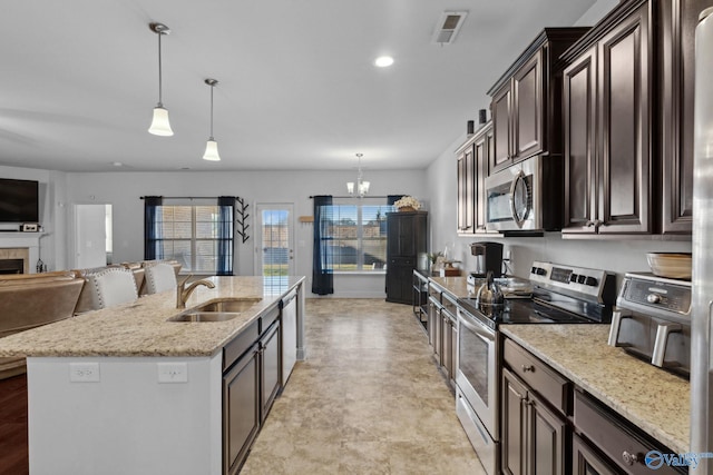 kitchen featuring dark brown cabinetry, stainless steel appliances, sink, pendant lighting, and a fireplace