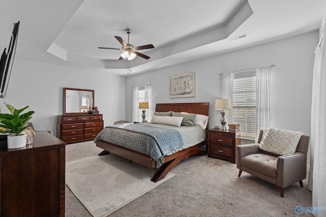 carpeted bedroom with a tray ceiling, multiple windows, and ceiling fan