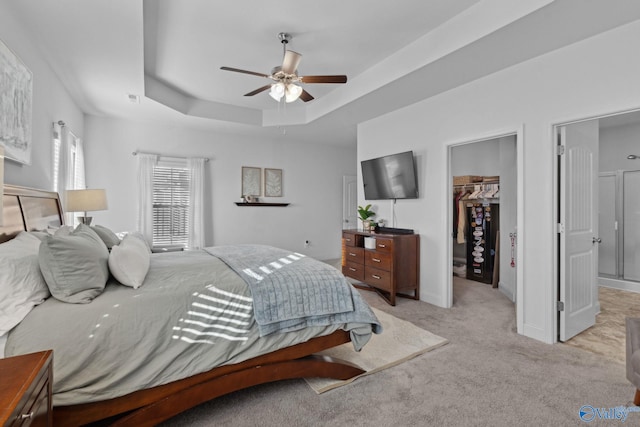 bedroom with a raised ceiling, a walk in closet, ceiling fan, light colored carpet, and a closet