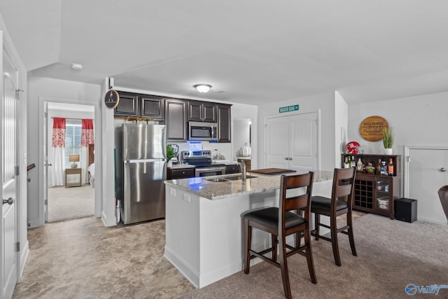 kitchen with a kitchen bar, light stone countertops, stainless steel appliances, sink, and a center island with sink