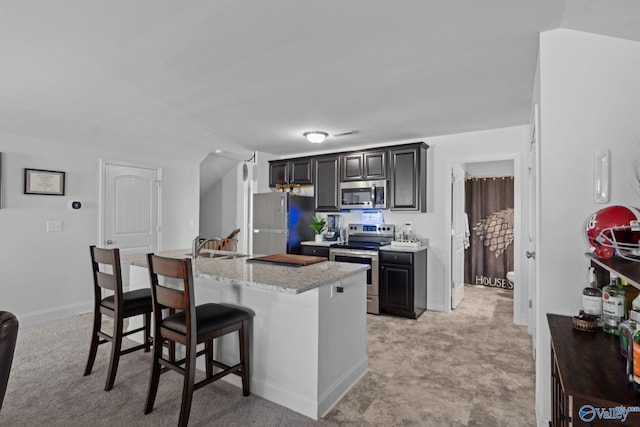 kitchen featuring light stone counters, light colored carpet, a breakfast bar area, and appliances with stainless steel finishes