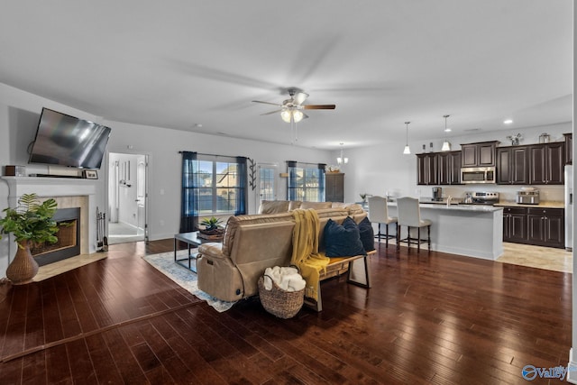 living room featuring a tiled fireplace, ceiling fan, and dark wood-type flooring