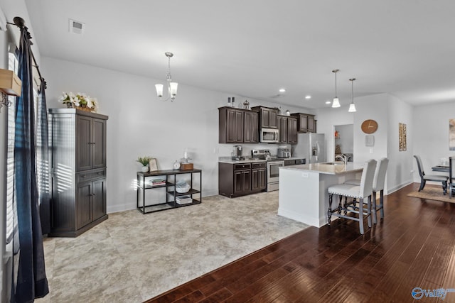 kitchen with dark brown cabinetry, stainless steel appliances, light hardwood / wood-style flooring, decorative light fixtures, and a kitchen island with sink