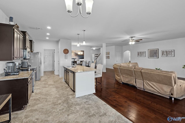 kitchen featuring dark brown cabinets, stainless steel appliances, pendant lighting, a center island with sink, and light hardwood / wood-style floors