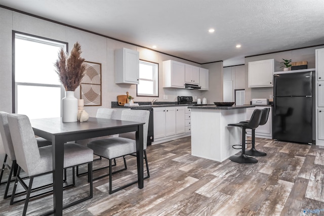 kitchen with black fridge, white cabinetry, a kitchen breakfast bar, and a kitchen island