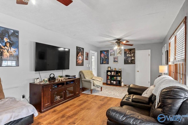 living room featuring ceiling fan, light hardwood / wood-style flooring, and a textured ceiling