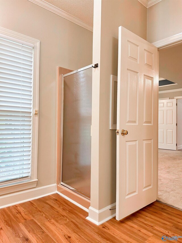 bathroom with a shower with shower door, wood finished floors, baseboards, and ornamental molding
