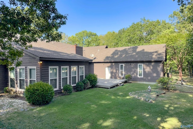 rear view of house with a lawn, a wooden deck, roof with shingles, and a chimney