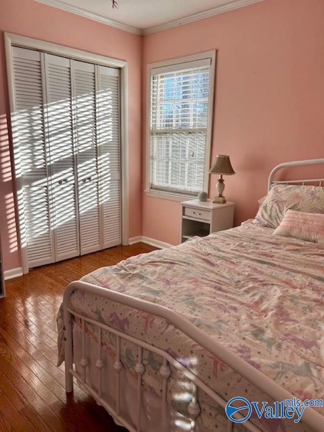 bedroom with a closet, wood-type flooring, and ornamental molding