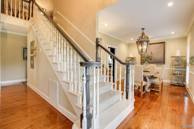 staircase with hardwood / wood-style flooring, crown molding, baseboards, and visible vents