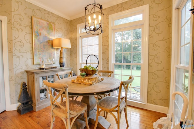 dining room with light wood finished floors, wallpapered walls, baseboards, ornamental molding, and an inviting chandelier