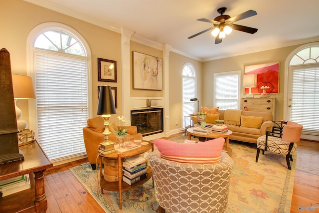 living room with a glass covered fireplace, light wood-style flooring, ceiling fan, and ornamental molding