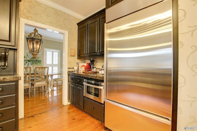 kitchen with light wood finished floors, dark brown cabinets, wallpapered walls, ornamental molding, and appliances with stainless steel finishes