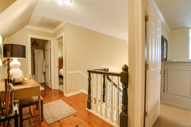 hallway with an upstairs landing, lofted ceiling, wood-type flooring, and crown molding