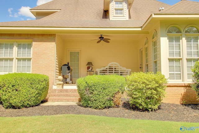 entrance to property with brick siding, ceiling fan, and a shingled roof