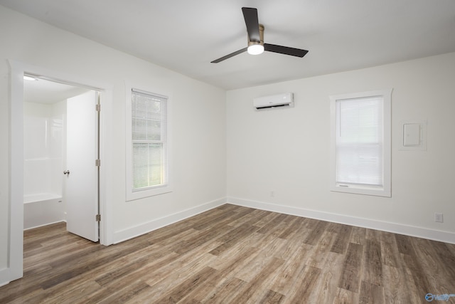 empty room featuring a wall unit AC, wood finished floors, a ceiling fan, and baseboards
