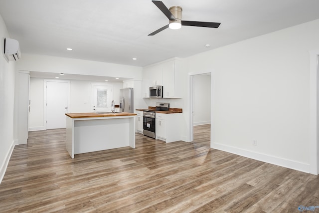 kitchen featuring wood counters, stainless steel appliances, a wall mounted AC, white cabinets, and light wood-style floors