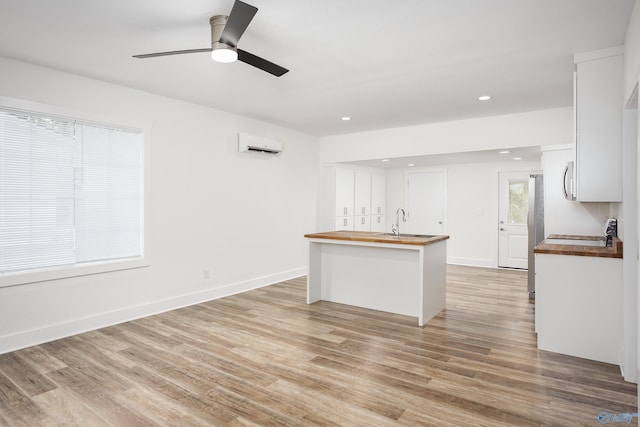 kitchen with wooden counters, a wall mounted AC, light wood-style flooring, white cabinetry, and recessed lighting