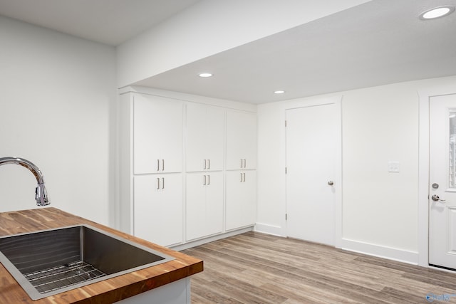 kitchen with a sink, butcher block counters, recessed lighting, light wood-style flooring, and white cabinets
