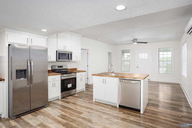 kitchen featuring appliances with stainless steel finishes, wood counters, a sink, light wood-style floors, and white cabinetry