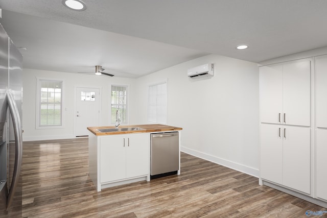 kitchen featuring butcher block counters, appliances with stainless steel finishes, a wall mounted AC, a sink, and baseboards