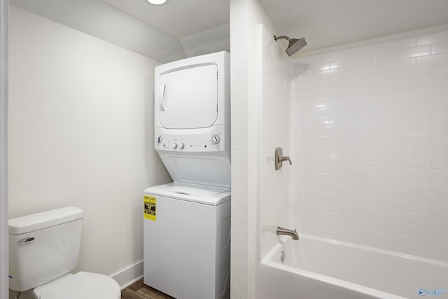 bathroom featuring stacked washer / drying machine, toilet,  shower combination, wood finished floors, and baseboards