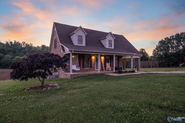 cape cod home featuring covered porch and a lawn