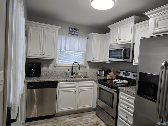 kitchen featuring white cabinetry, appliances with stainless steel finishes, sink, and light stone counters