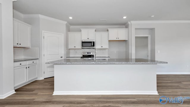 kitchen with light stone countertops, appliances with stainless steel finishes, an island with sink, hardwood / wood-style floors, and white cabinetry