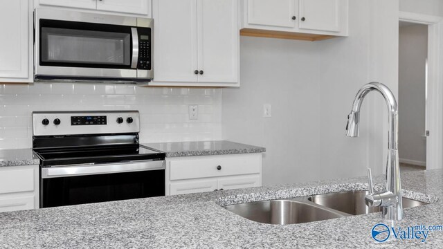 kitchen with stainless steel appliances, light stone countertops, sink, and white cabinets