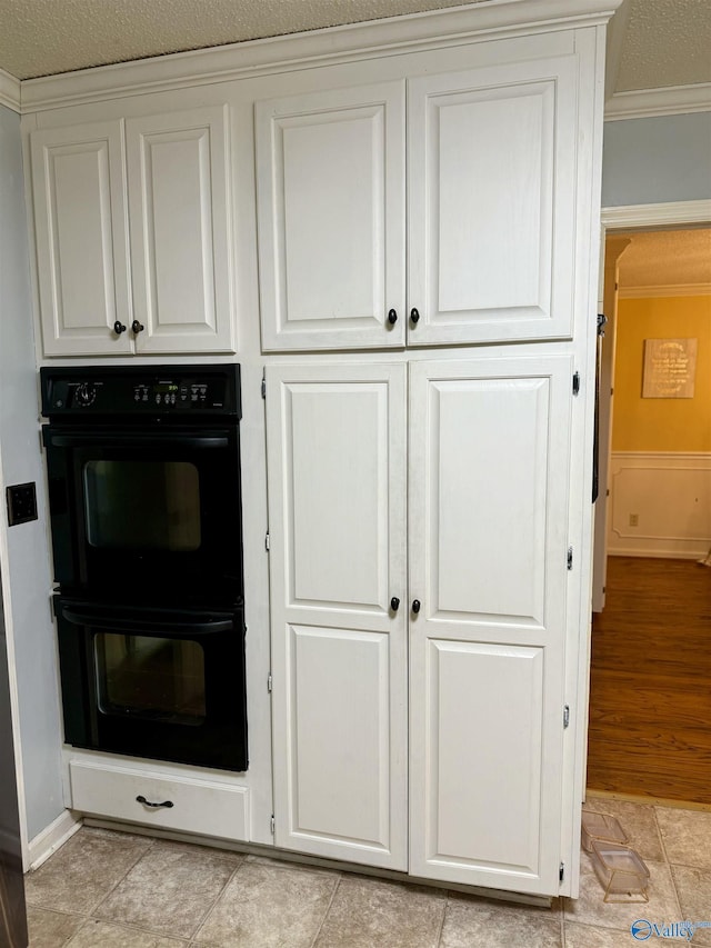 kitchen featuring a textured ceiling, white cabinetry, double oven, and ornamental molding