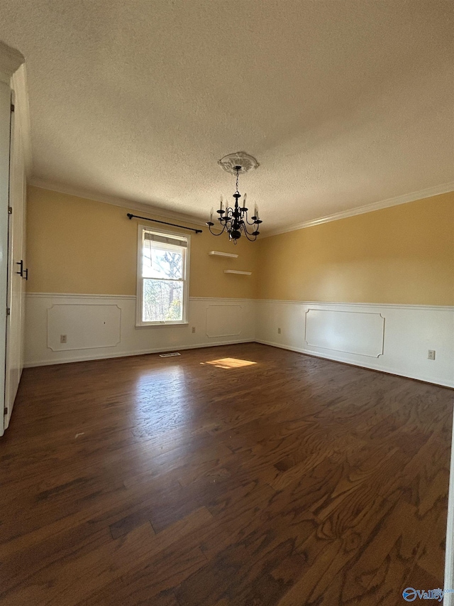 empty room with dark hardwood / wood-style flooring, a chandelier, a textured ceiling, and ornamental molding