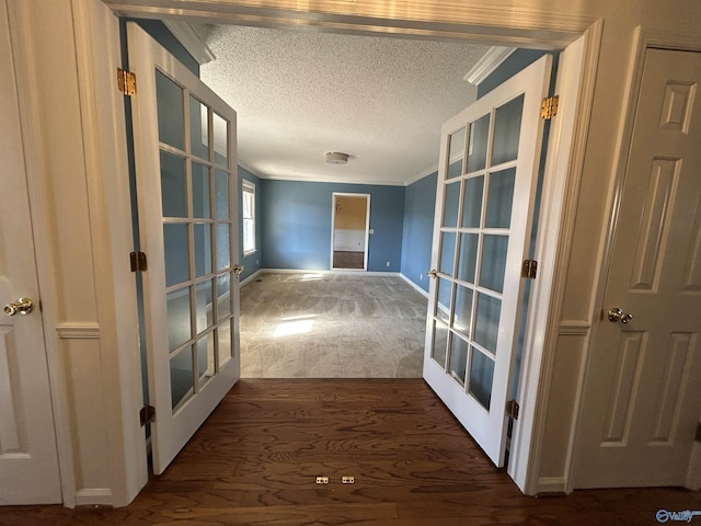 corridor with french doors, ornamental molding, a textured ceiling, and dark colored carpet