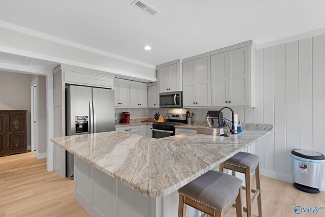 kitchen featuring light wood-type flooring, kitchen peninsula, appliances with stainless steel finishes, and a breakfast bar area