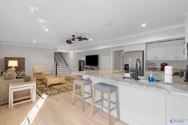 kitchen featuring light hardwood / wood-style floors, a breakfast bar area, appliances with stainless steel finishes, light stone countertops, and white cabinets