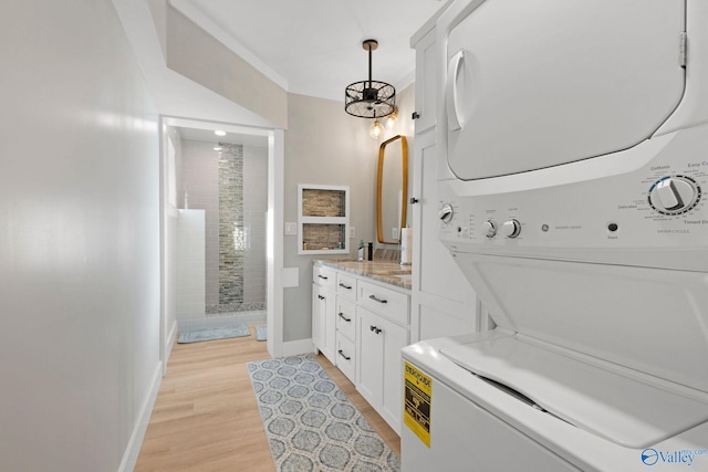 bathroom featuring vanity, stacked washer and dryer, an inviting chandelier, hardwood / wood-style flooring, and tiled shower