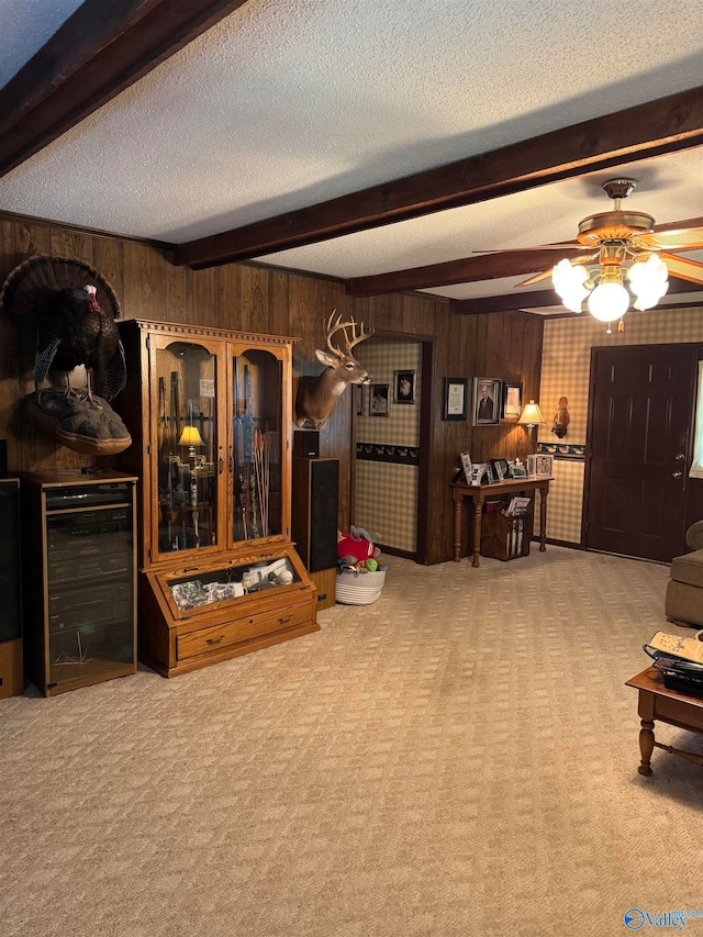 living room with wood walls, ceiling fan, a textured ceiling, beam ceiling, and carpet floors